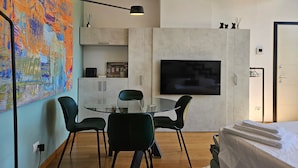 A modern room with a glass dining table, black chairs, a flat-screen TV, and a large abstract painting on the wall.