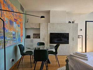 Une pièce moderne avec une table à manger en verre, des chaises noires, un téléviseur à écran plat et un grand tableau abstrait accroché au mur.