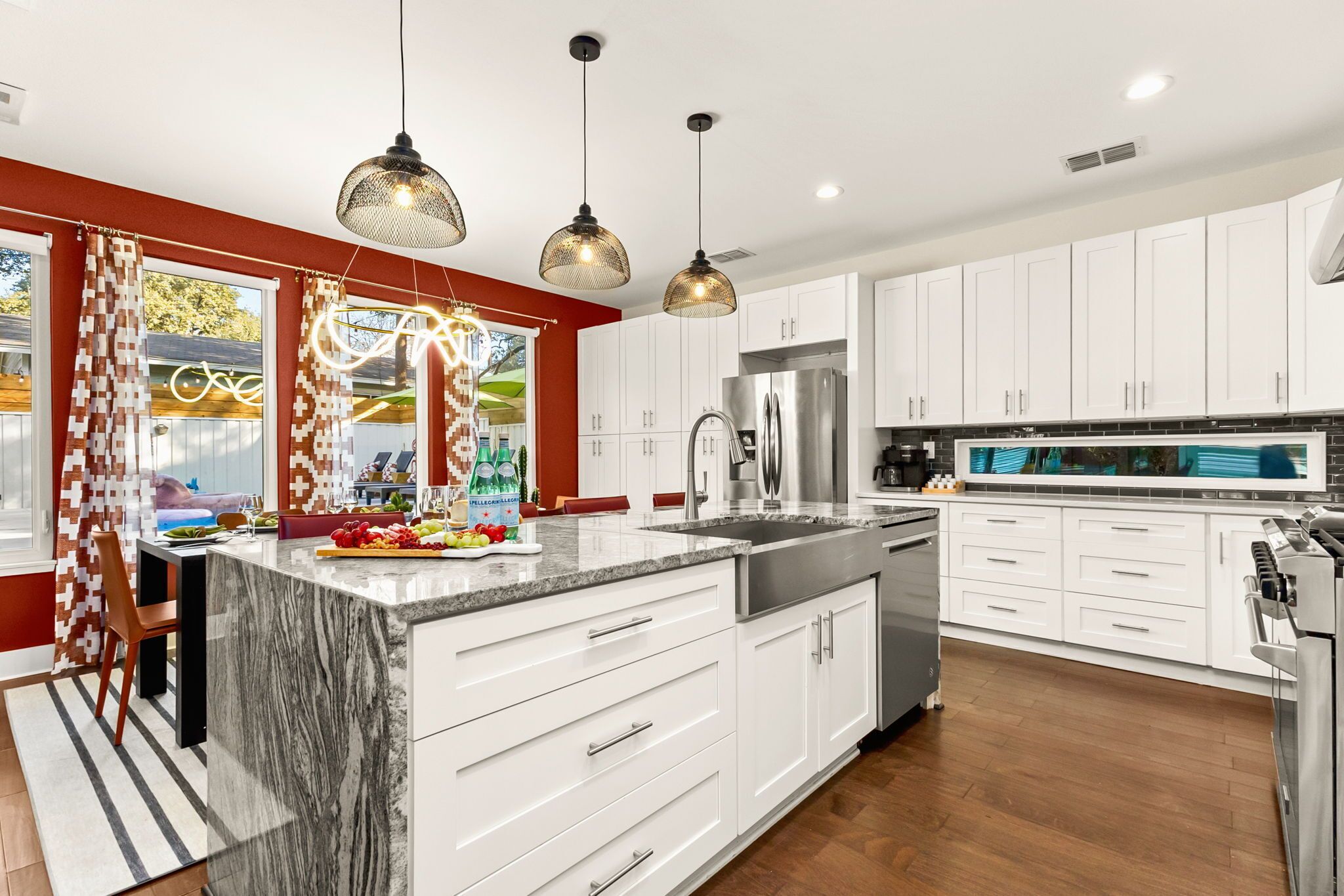 A modern kitchen with white cabinets, a large island, stainless steel appliances, and pendant lighting.