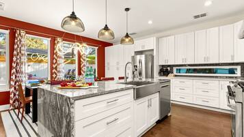 A modern kitchen with white cabinets, a large island, stainless steel appliances, and pendant lighting.