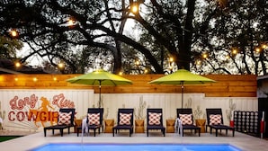 A pool area with lounge chairs and umbrellas, surrounded by wooden walls and string lights. - Heated Pool, MiniGolf, Karaoke, Game Room, Spa, 2mi to DT - SoCo Cowgirl (Austin)