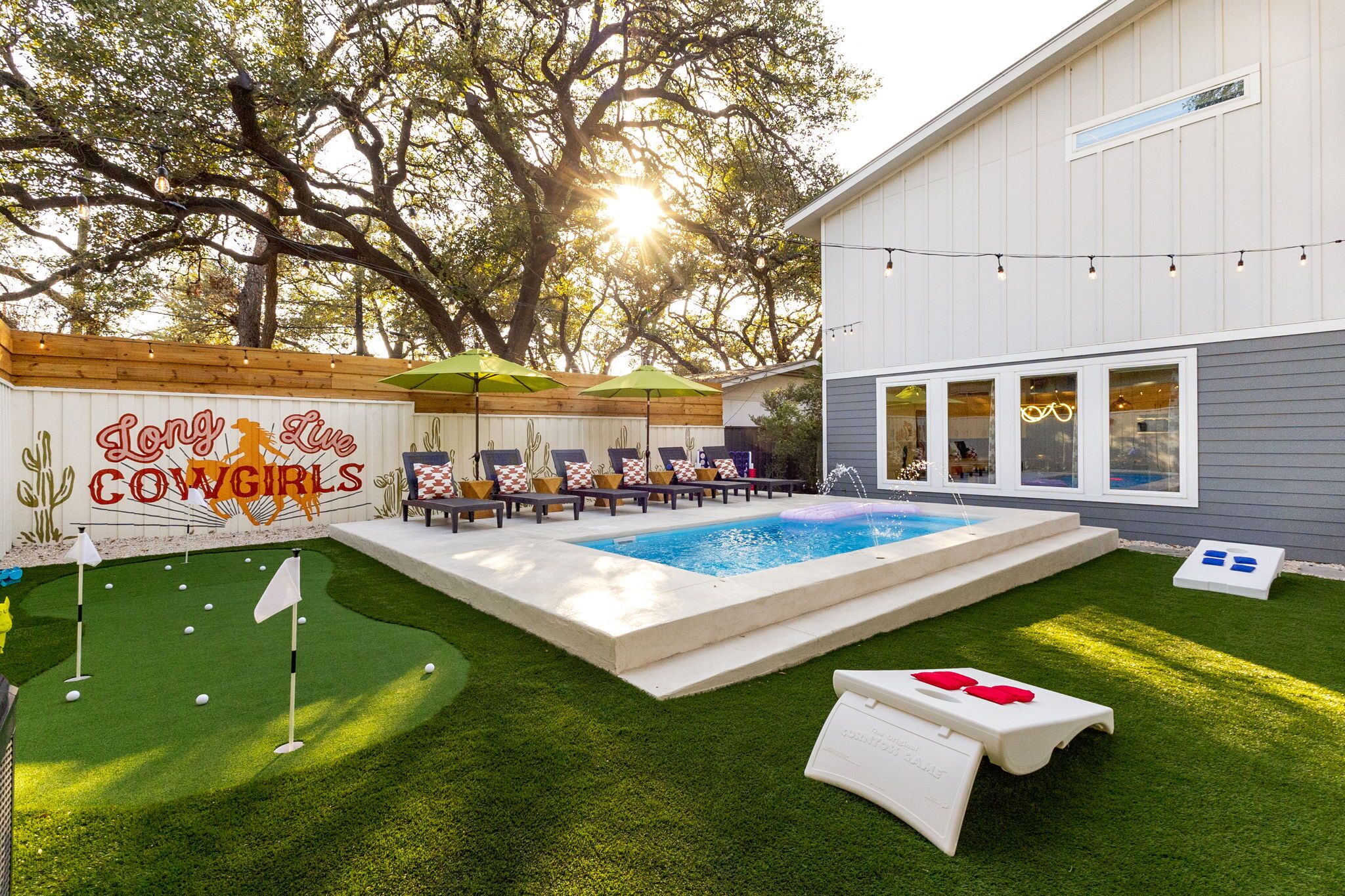 Un patio trasero con piscina, un área de patio con sillas y sombrillas, y un letrero que dice 'Long Live Cowgirls'.