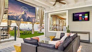 A modern outdoor living area with a large screen displaying Paramount branding, a comfortable seating arrangement, and a mounted TV showing streaming services. - Heated Pool, MiniGolf, Karaoke, Game Room, Spa, 2mi to DT - SoCo Cowgirl (Austin)