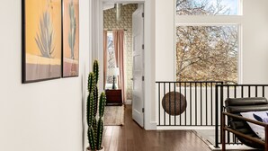 A hallway with a cactus, a door leading to a room with a view of trees, and a balcony with a railing. - Heated Pool, MiniGolf, Karaoke, Game Room, Spa, 2mi to DT - SoCo Cowgirl (Austin)