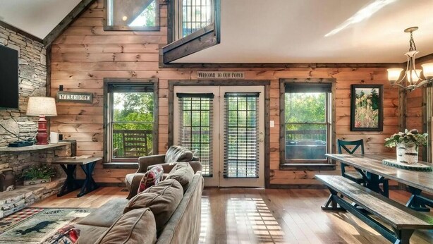 A cozy cabin interior with a wooden exterior, a welcoming porch sign, a sofa, a dining table, and a bench. - 10 mins to Dollywood, Stunning Views, Open Space & HotTub, Pet (Pigeon Forge)