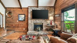 A cozy living room with a stone fireplace, wooden walls, a flat-screen TV, and comfortable seating. - 10 mins to Dollywood, Stunning Views, Open Space & HotTub, Pet (Pigeon Forge)