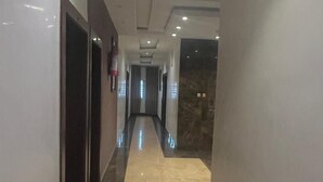 Moderni hotellikäytävä, jossa on marmorilattia, upotetut valaisimet ja seinällä palosammutin.