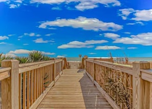 A wooden boardwalk leading to a beach with a clear sky.