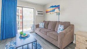 A living room with a brown sofa, a blue curtain, a small table with a plant, and a painting on the wall. - Sea Mist 50504 (Myrtle Beach)
