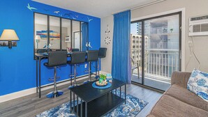 A modern living room with a dining area, a balcony with a view, and a blue accent wall. - Sea Mist 50504 (Myrtle Beach)
