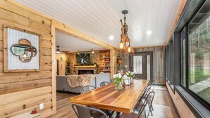 A wooden interior with a long dining table, chairs, and a chandelier. - Two Creeks Lodge Modern Creekfront Stay King beds (Cherry Log)