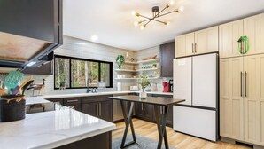 A modern kitchen with a central island, wooden cabinets, and a large window providing natural light. - Two Creeks Lodge Modern Creekfront Stay King beds (Cherry Log)