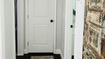 Un couloir avec une porte blanche, un tapis à motifs et une porte rustique sur la droite.