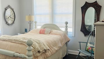 Une chambre à coucher comprenant un lit, une commode, un fauteuil à bascule, un lustre, une fenêtre avec des stores et une horloge murale.