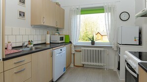 A kitchen with wooden cabinets, a microwave, a dishwasher, a window with curtains, and a clock on the wall. - 1 bedroom beautiful home in Højer (Højer)