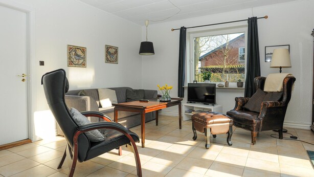 A living room with a sofa, a black leather chair, a wooden coffee table, a television, and a window with curtains. - 1 bedroom beautiful home in Højer (Højer)