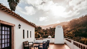 Una terraza con un muro blanco, suelo de baldosas y vistas a un paisaje montañoso.