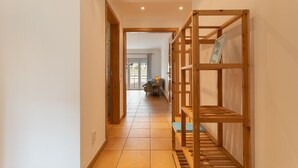 A hallway with a wooden bench, a door leading to a room, and a view of a living area with a sofa and a lamp. - Sesimbra Beach Apartment by GT House (Sesimbra)