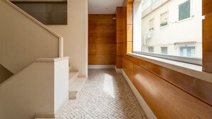 A narrow hallway with a tiled floor, a wooden wall, and a window overlooking a building with balconies. - Sesimbra Beach Apartment by GT House (Sesimbra)