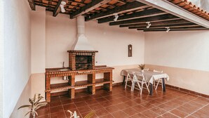 Um pátio com forno de tijolos, mesa e cadeiras, e um vaso com planta.