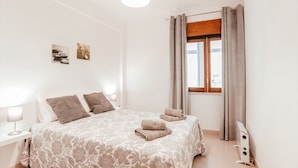 Quarto bem arrumado com cama grande, duas mesinhas de cabeceira, janela com cortinas e decoração na parede.