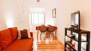 Ett vardagsrum med en soffa, ett matbord med stolar, en tv på ett tv-bord och en hängande lampa.