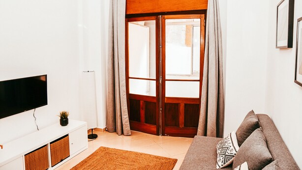 A living room with a flat-screen TV, a white cabinet, a brown woven rug, and a brown sofa with patterned cushions. - Giestal Terrace By GT House (Lisbon)