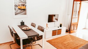 A dining area with a white table, black chairs, a brown rug, a television, and a cabinet with a plant. - Giestal Terrace By GT House (Lisbon)