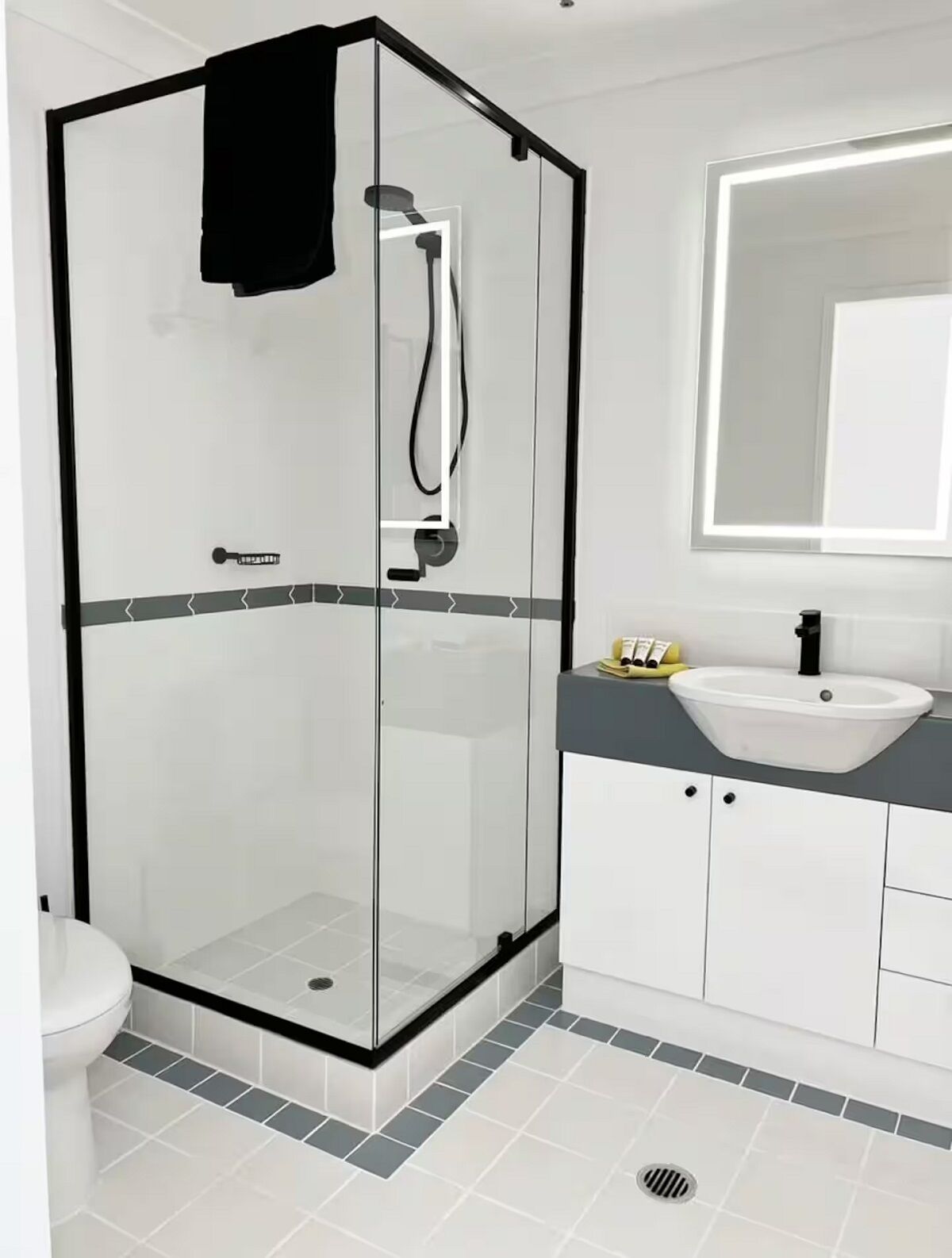 Un baño moderno con ducha de vidrio, lavabo blanco y un espejo grande sobre el lavabo.