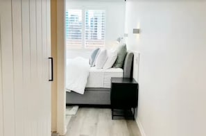 A modern bedroom with a bed, bedside table, and a window with blinds. -  Studio apartment with City Views (Kangaroo Point)