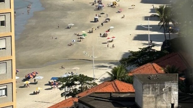Una spiaggia con persone e ombrelloni, uno skyline cittadino sullo sfondo e edifici con tetti rossi in primo piano.