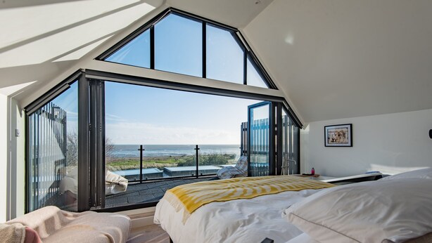 A bedroom with a large skylight, a bed with white bedding, and a view of the ocean.