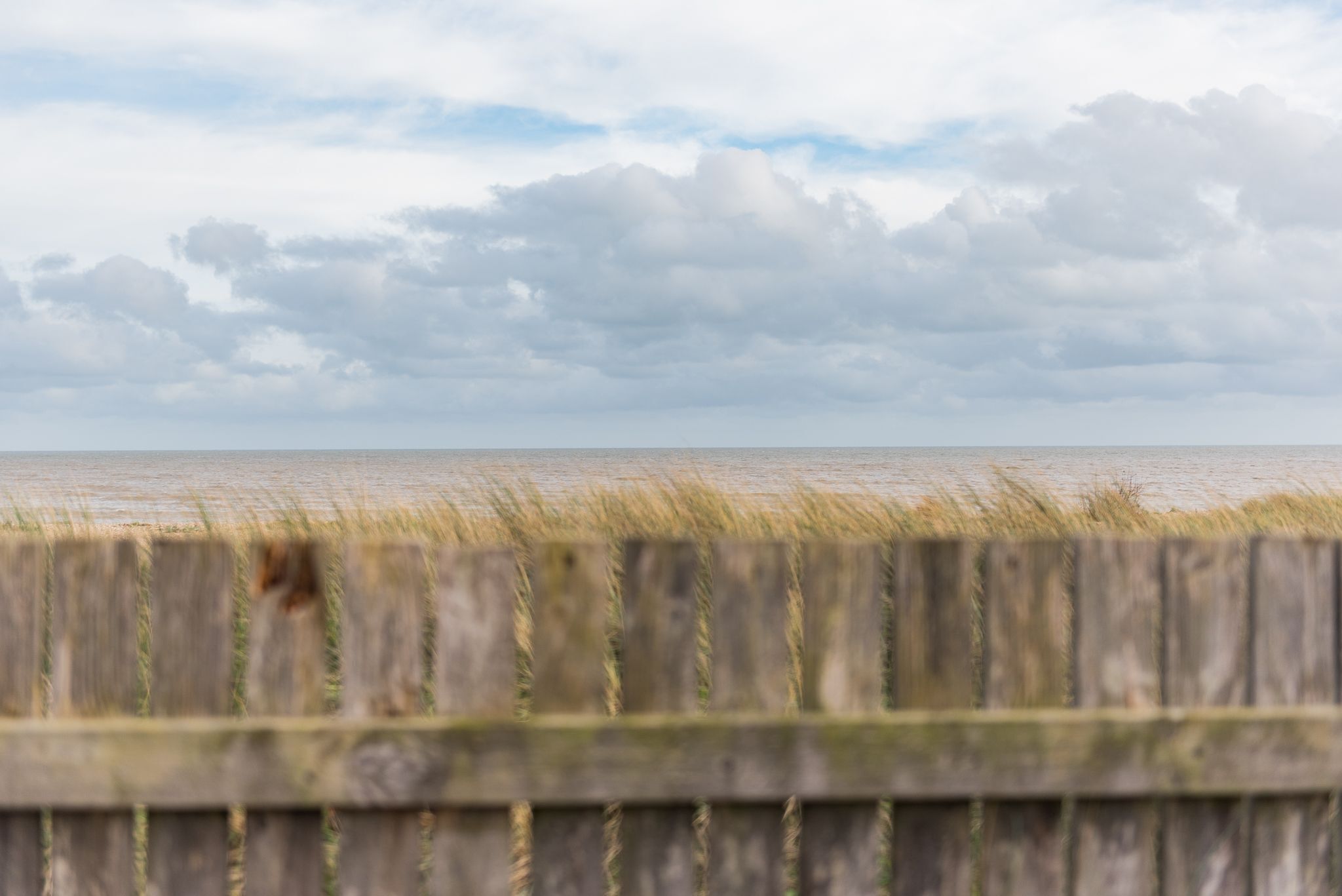 Une clôture en bois offrant une vue sur la mer et un ciel nuageux.