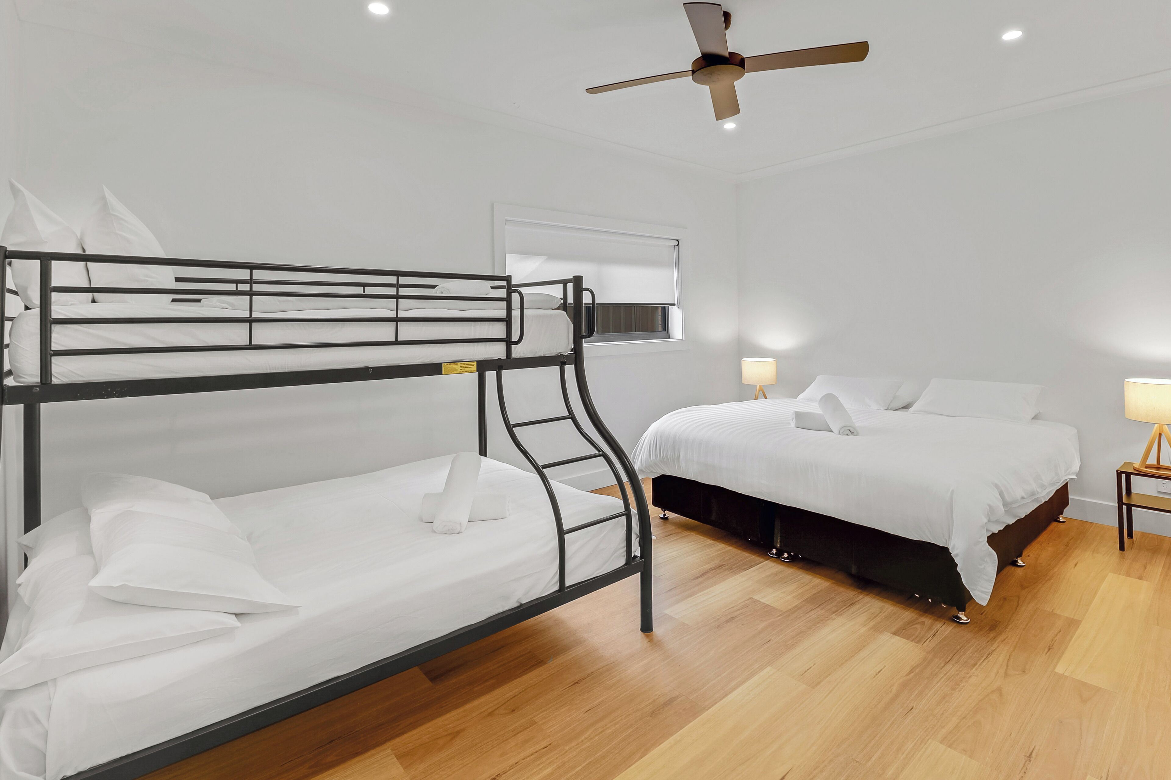 Habitación con literas, ventilador de techo, ventana con persianas y mesita de noche con lámpara.