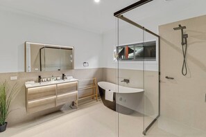 A modern bathroom with a glass shower enclosure, a freestanding bathtub, and a vanity with a mirror. - The Calzburg  (Mansfield)