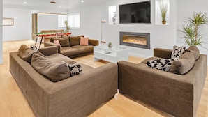 Una sala de estar moderna con sofás marrones, una mesa de centro blanca, una chimenea y un televisor montado en la pared.
