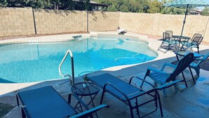 A swimming pool with a tiled deck, surrounded by lounge chairs and a table.