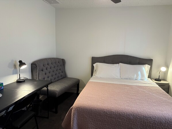 Una habitación de hotel con cama, escritorio, silla y mesita de noche con lámpara.