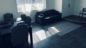 A living room with a dining table, chairs, a sofa, a rug, and a window with sheer curtains.