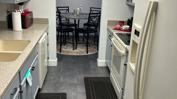 A compact kitchen with grey cabinets, a white refrigerator, a microwave, and a dining area with a table and chairs.