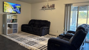 A living room with a black sofa, a white entertainment unit, a ceiling fan, and a large TV displaying a scenic landscape.