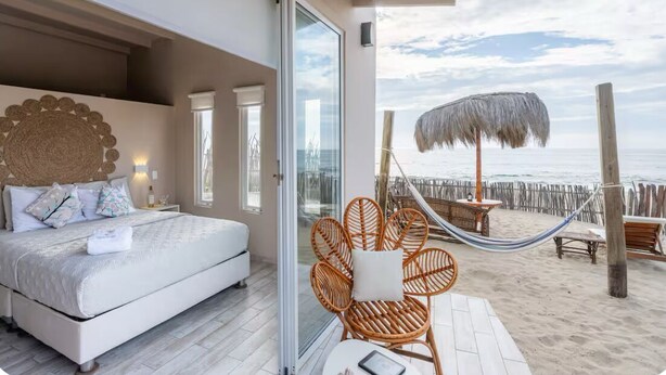 Ein Schlafzimmer mit einem großen Bett, einer Glastür, die auf einen Balkon führt, und Blick auf den Strand.
