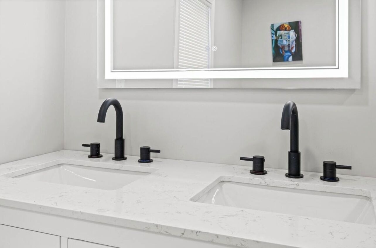 Une salle de bain avec deux lavabos, chacun doté d’un robinet noir, et un grand miroir au-dessus.
