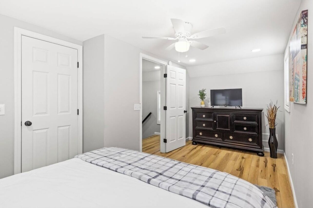 A bedroom with a bed, a dresser, a ceiling fan, and a TV.