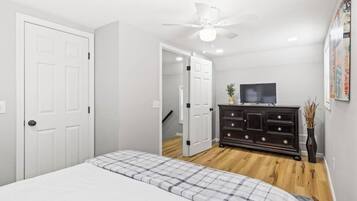 A bedroom with a bed, a dresser, a ceiling fan, and a TV.