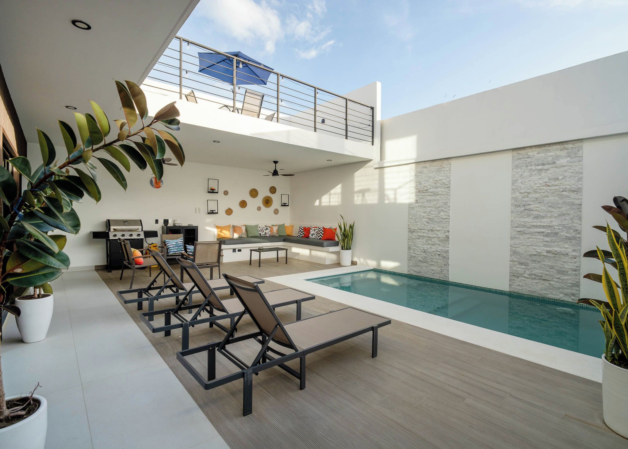A modern outdoor living area with a pool, lounge chairs, a dining table, and a kitchen area.