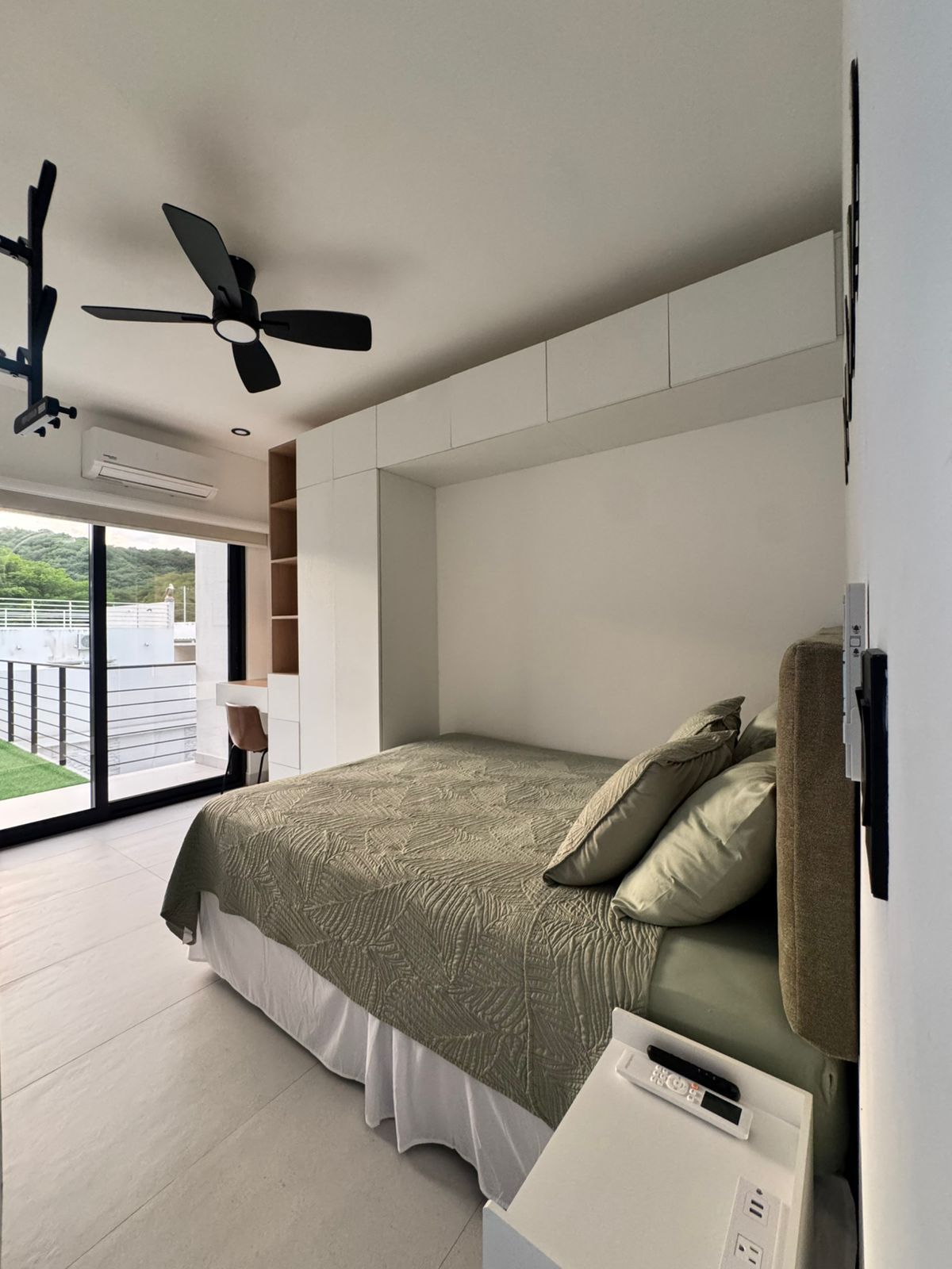 A modern bedroom with a large bed, a ceiling fan, and a view of a balcony.