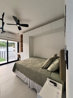 A modern bedroom with a large bed, a ceiling fan, and a view of a balcony.