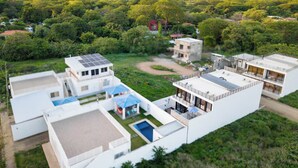 A modern residential complex with multiple buildings, a swimming pool, and a surrounding green landscape. - Ocean Dream Apartments E2-B4 (San Juan del Sur)