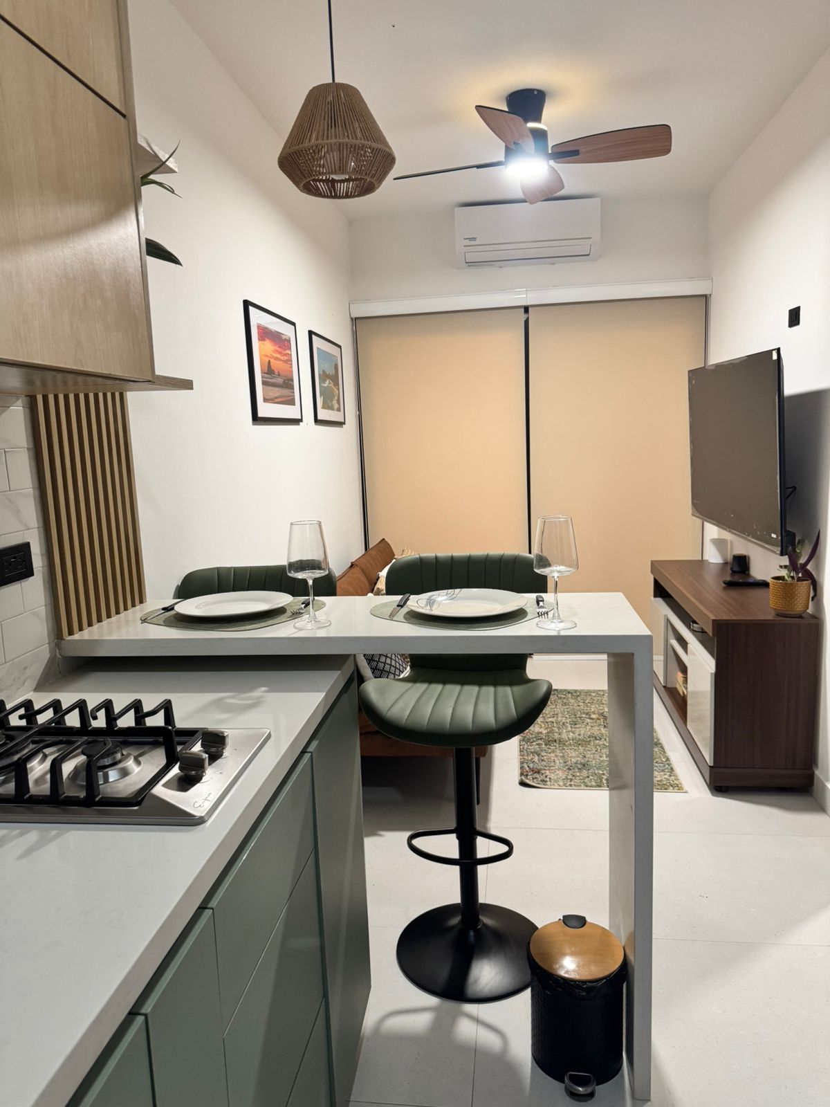 A compact kitchen with a gas stove, a dining table with two chairs, a ceiling fan, and a television on a stand.
